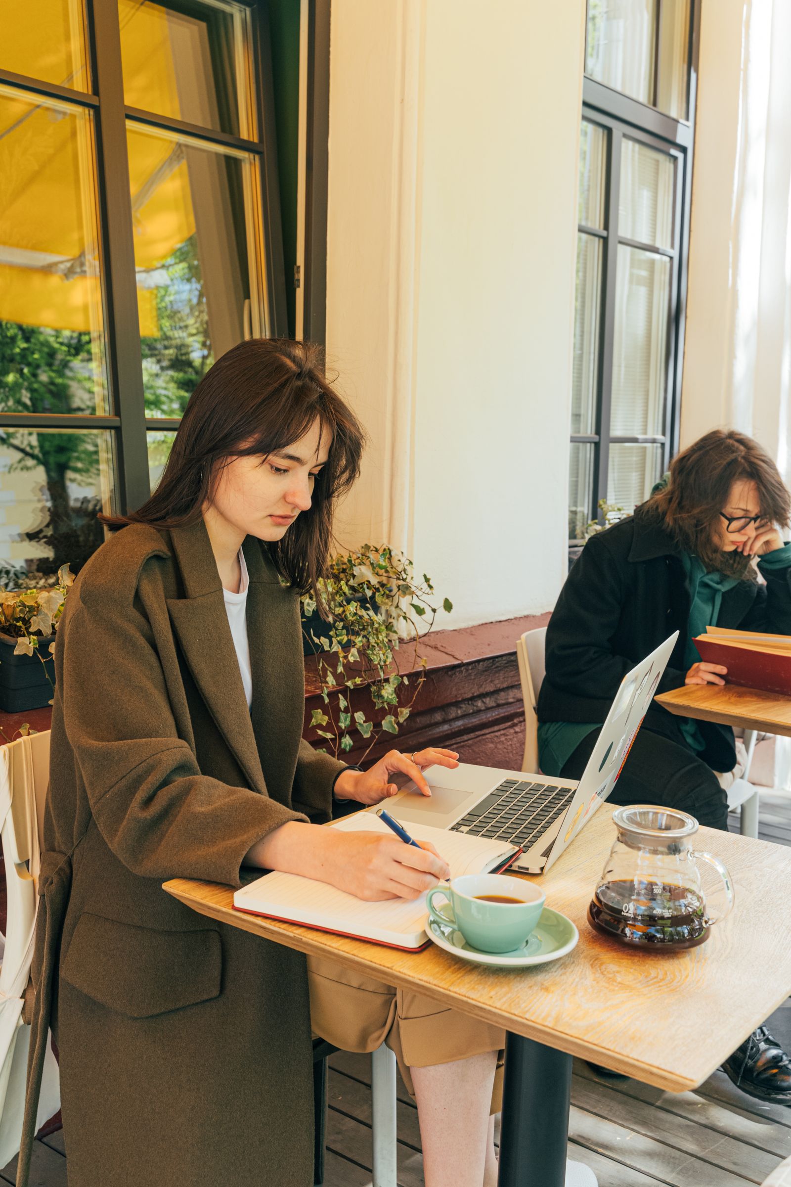 Small-business owner planning work at a cafe with her laptop and notebook